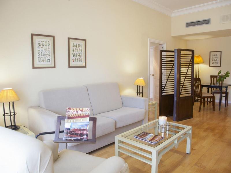 Gezellige hotelkamer met bank, glazen salontafel, lampen en stijlvolle houten scheidingswand.