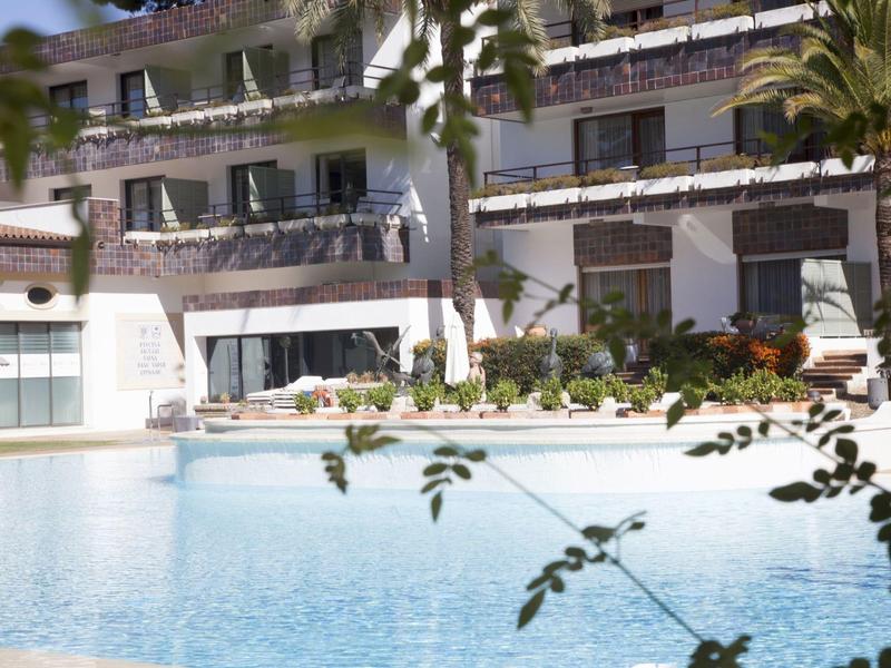 Hotelgebouw met balkons kijkt uit op een helder zwembad omringd door planten.