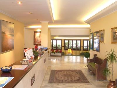 Ingresso di hotel luminoso con banco della reception, panca e tappeto.