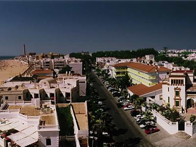 Città costiera con spiaggia sabbiosa, strade ed edifici storici sotto un cielo scuro e nuvoloso.