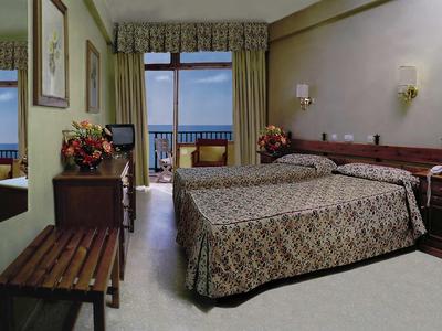 Camera d'hotel con due letti singoli, balcone e vista mare, arredata in modo accogliente.