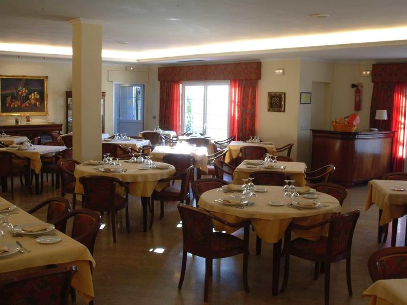 Accogliente sala da pranzo con tavoli rotondi, sedie, luce calda e tende.