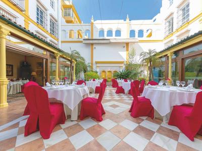 Outdoor restaurant seating with tables and red covered chairs in a bright courtyard.