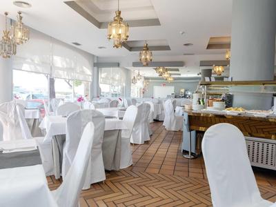 Spacious restaurant with white-covered chairs, chandeliers, and herringbone wooden floor.