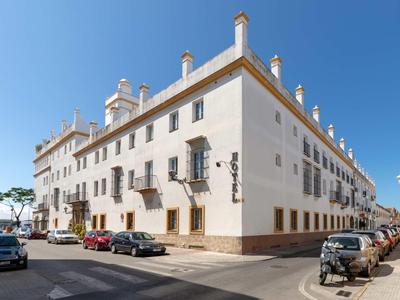Large white hotel building with brown trim under a clear blue sky on a corner street.