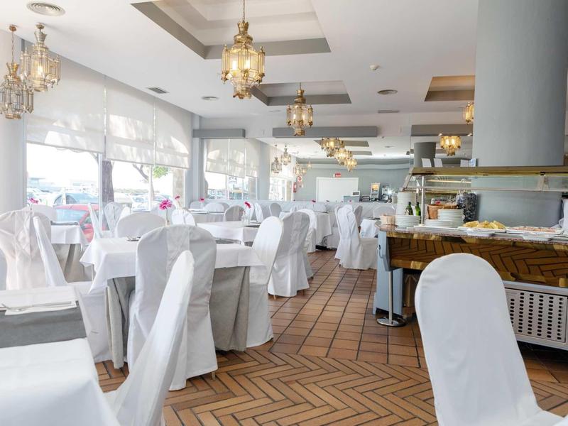 Spacious restaurant with white-covered chairs, chandeliers, and herringbone wooden floor.