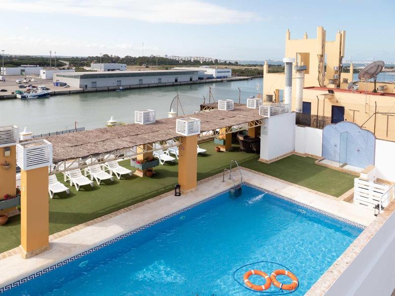 Rooftop swimming pool with lounge chairs overlooking a harbor with boats and buildings.