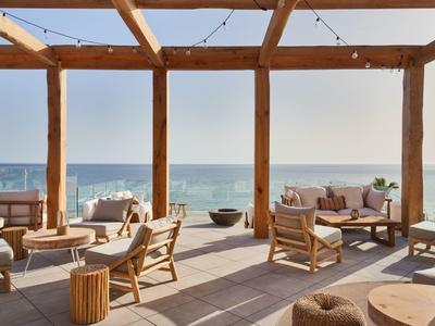 Moderní venkovní posezení s pohodlným nábytkem a výhledem na moře pod dřevěnou pergolou.