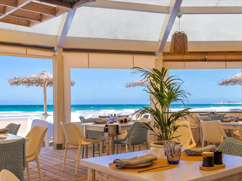 Světlá, vzdušná restaurace s výhledem na písečnou pláž a modré moře.