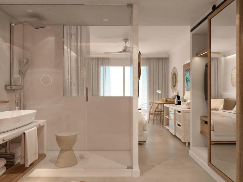 Moderní hotelový pokoj se skleněnou sprchou, postelí a skříní odrážející teplé světlo.