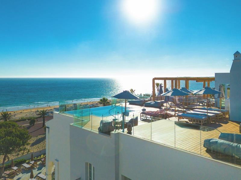 Hotelová terasa u moře s lehátky, slunečníky, modrým bazénem a jasnou oblohou.