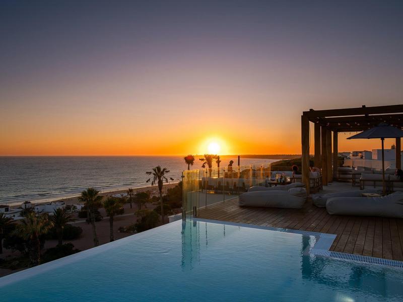 Západ slunce nad nekonečným bazénem a oceánem v luxusním přímořském resortu.