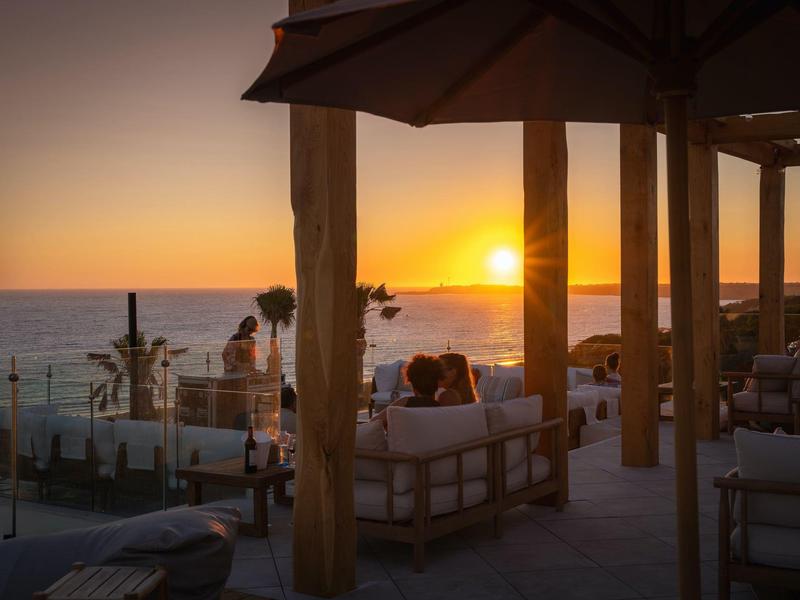 Výhled na západ slunce v přímořském salonku s pohodlným posezením a slunečníky.