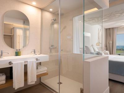 Modernes Hotelzimmer mit weißem Badezimmer, offener Dusche und Blick auf das Schlafzimmer.