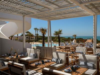 Offener Loungebereich mit modernen Sitzmöbeln, Blick auf Pool, Palmen und Meer bei Sonnenschein.