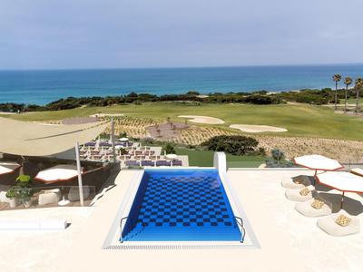 Infinity bazén s modrou vodou s výhledem na golfové hřiště a moře za jasné oblohy.