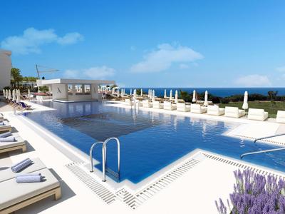 Moderní hotelový bazén s bílými lehátky a výhledem na modré moře pod jasnou oblohou.