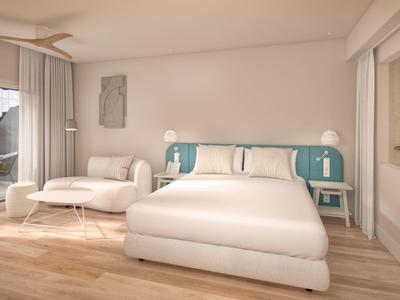 Světlý hotelový pokoj s velkou postelí, pohovkou a dřevěnou podlahou.