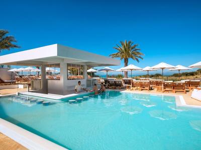 Moderner Hotelpool mit Bar, Sonnenschirmen und Palmen unter klarem blauem Himmel.