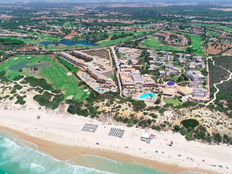Letecký pohled na resort s bazény, golfovým hřištěm a písečnou pláží u moře.
