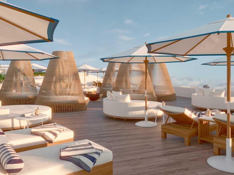 Terrazza sulla spiaggia luminosa e moderna con lettini, grandi ombrelloni e sedie sospese intrecciate.