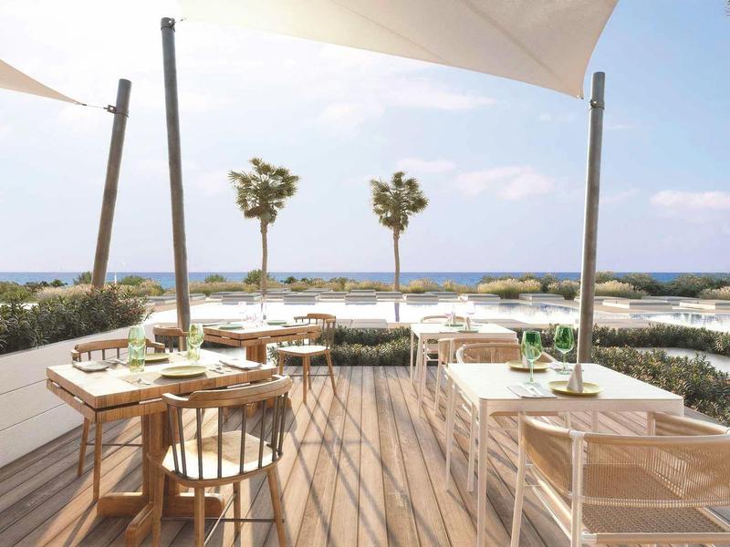 Terasa s dřevěnou podlahou, stolem a židlemi s výhledem na moře a palmy.