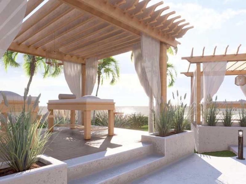 Zastřešené venkovní masážní oblasti s výhledem na moře a palmami při západu slunce.