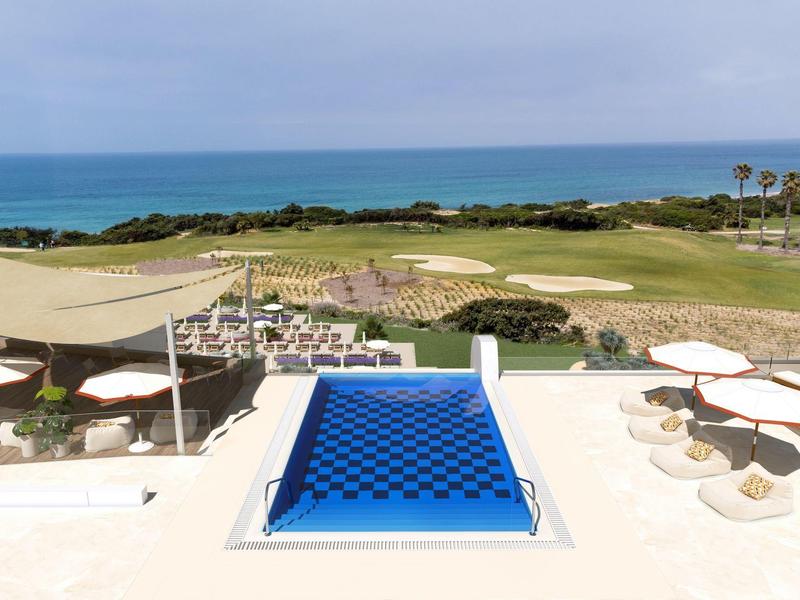 Infinity bazén s modrou vodou s výhledem na golfové hřiště a moře za jasné oblohy.