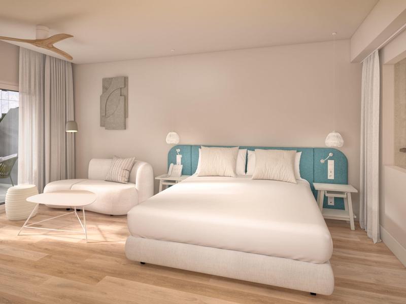 Světlý hotelový pokoj s velkou postelí, pohovkou a dřevěnou podlahou.