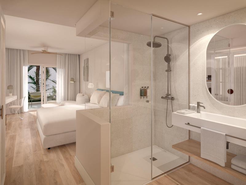 Moderní hotelový pokoj s pohodlnou postelí, skleněnou sprchou a výhledem na moře z okna.