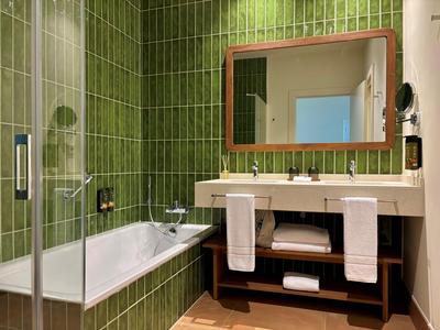 Modernes Badezimmer mit grünen Fliesen, Badewanne, Waschbecken und großen Spiegel.