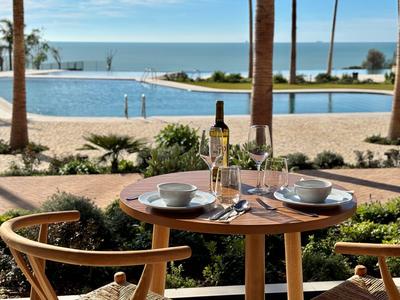 Ein gedeckter Tisch auf einer Terrasse mit Blick auf einen Pool und das Meer im Hintergrund.