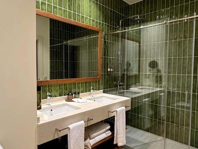 Modernes Badezimmer mit grün gefliester Dusche, Doppelwaschbecken und Holzregal mit Handtüchern.