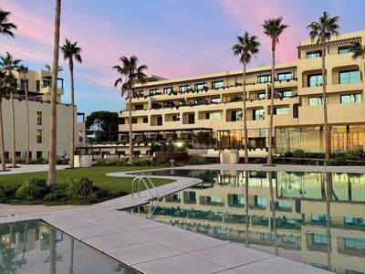 Modernes Hotel mit Pool und Palmen bei Sonnenuntergang unter blauem Himmel.