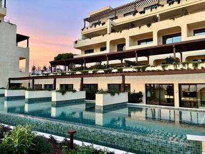 Moderner Hotelkomplex mit Pool und Terrassen vor Gebäude bei Sonnenuntergang.