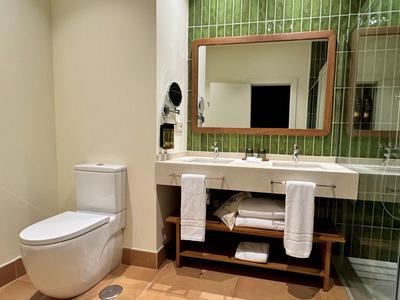 Modernes Badezimmer mit weißer Toilette, großem Spiegel und grün gekachelter Wand.