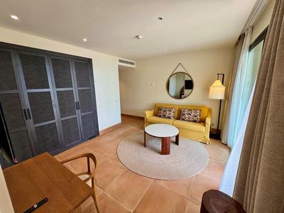 Helles Hotelzimmer mit gelbem Sofa, rundem Teppich, Couchtisch und dunklem Schrank.