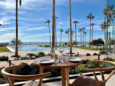 Tisch mit gedeckten Plätzen auf Terrasse mit Blick auf Pool, Palmen und Meer.