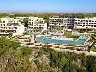 Modernes Hotel mit mehreren Gebäuden, großem Pool und umgebender grüner Landschaft, ideal für Urlaub.