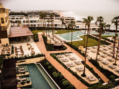 Moderner Hotelkomplex mit Pools, Liegestühlen und Palmen an der Küste.