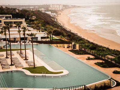 Luxuriöser Poolbereich mit Palmen neben einem langen Sandstrand am Meer.