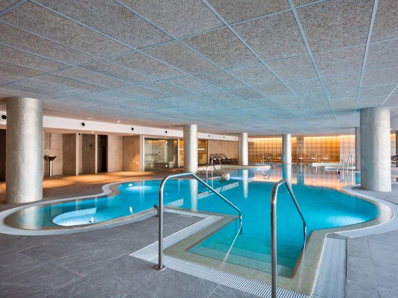 Piscina interna dell'hotel con design moderno e area salotto sullo sfondo.