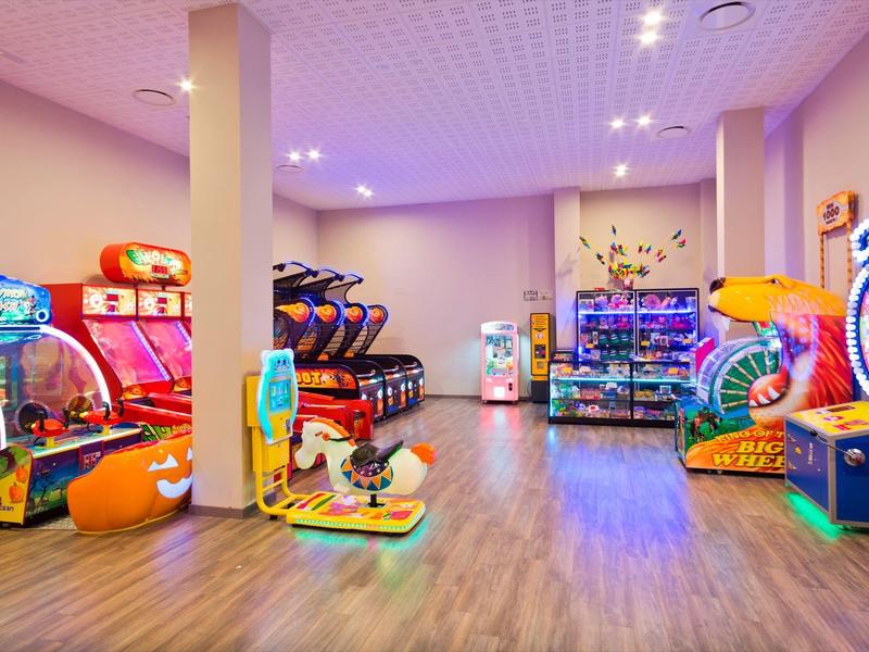 Sala giochi interna luminosa con varie macchine colorate su pavimento in legno.