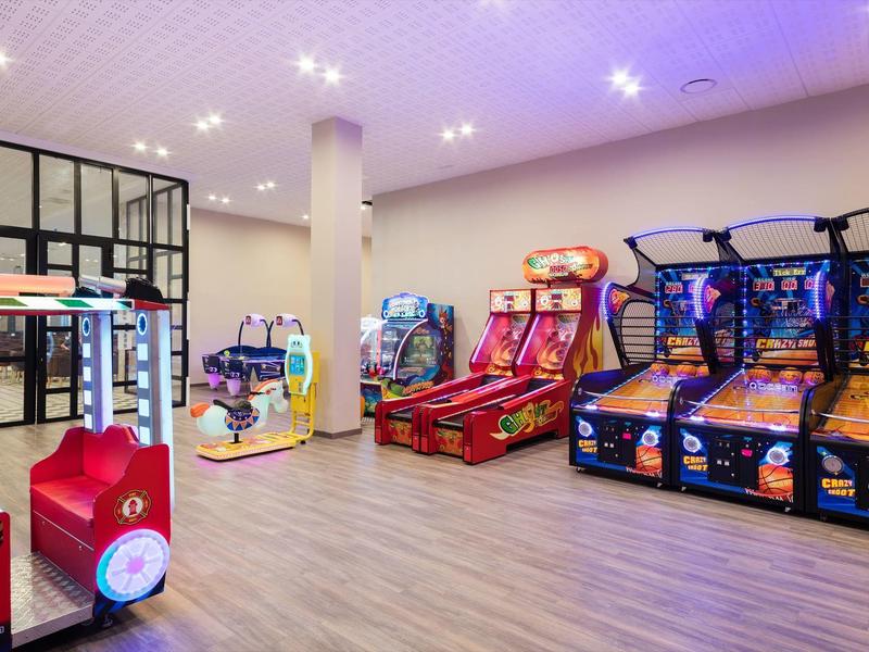 Sala giochi luminosa con vari colorati videogiochi e pavimento in legno.