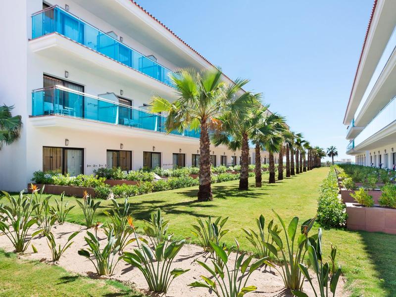 Hotel moderno con balconi, palme e giardino curato tra gli edifici.