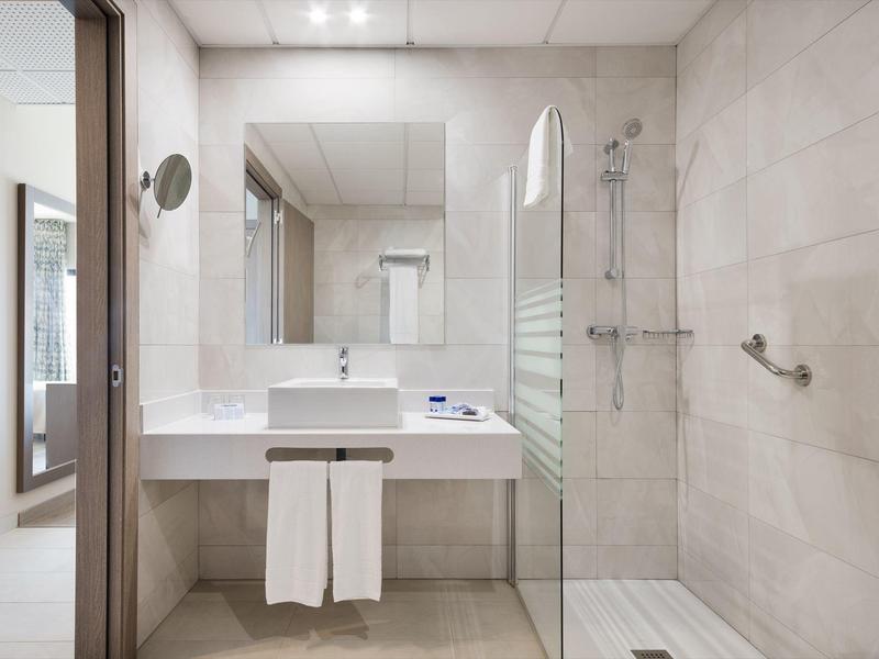 Bagno moderno in hotel con doccia a filo pavimento, grande specchio e lavabo bianco.