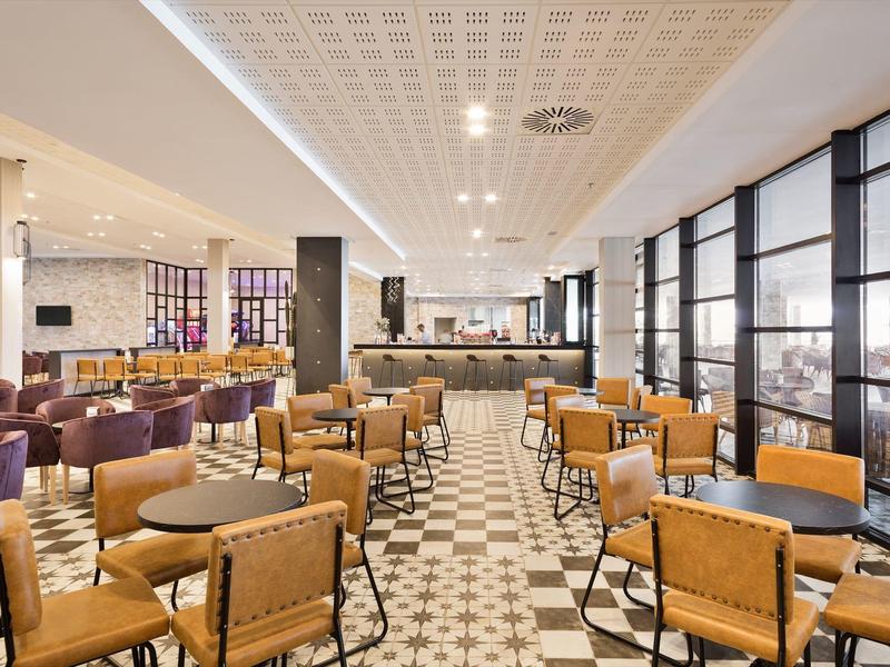 Caffè spazioso con pavimento decorato, sedie in pelle e tessuto, grandi finestre.