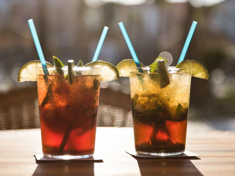 Due bicchieri di tè freddo con fette di limone e cannucce azzurre su una superficie in legno