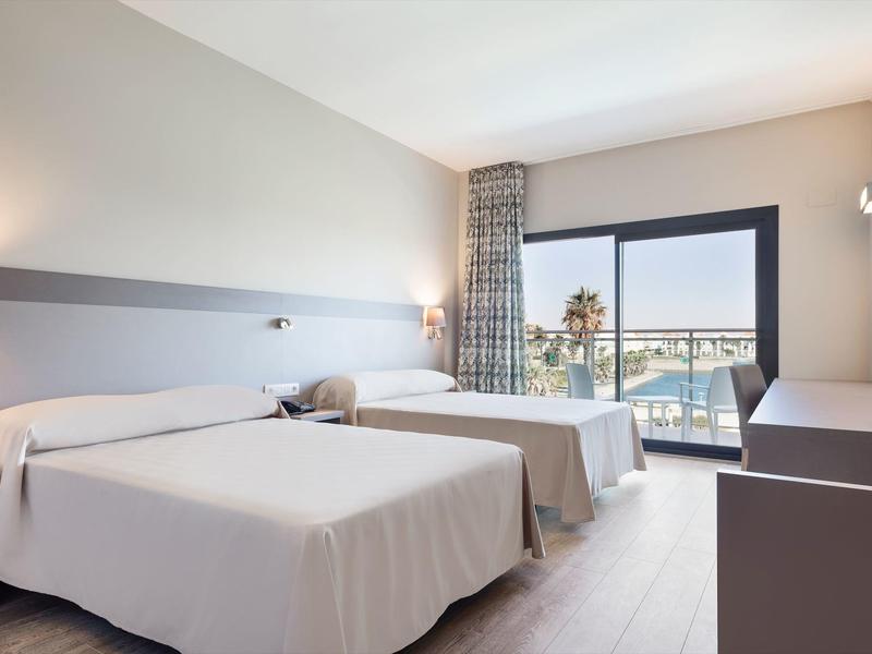 Camera d'hotel luminosa con due letti, porta finestra e vista sul balcone esterno.