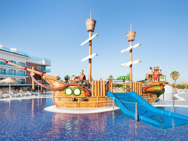 Piccola area gioco acquatica a tema pirata con scivoli in una piscina di un resort.